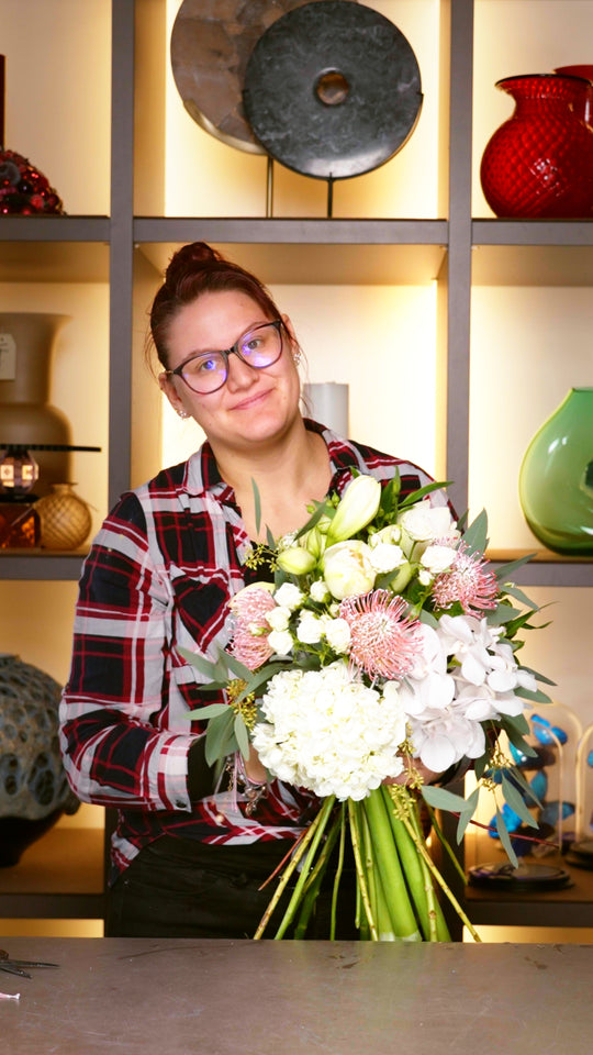 Blumen Bahlmann Mitarbeiterin Sally mit einem von ihr gebundenen Blumenstrauß aus weißen Hortensien, weißen Rosen, Amaryllis, Nadelkissen und Eukalyptus.