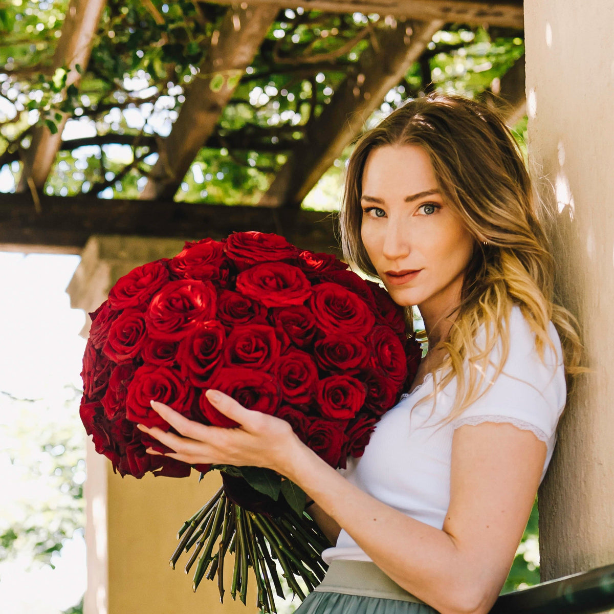 Frau hält im Rosengarten in München einen Blumenstrauß aus 50 roten Rosen zum Valentinstag.
