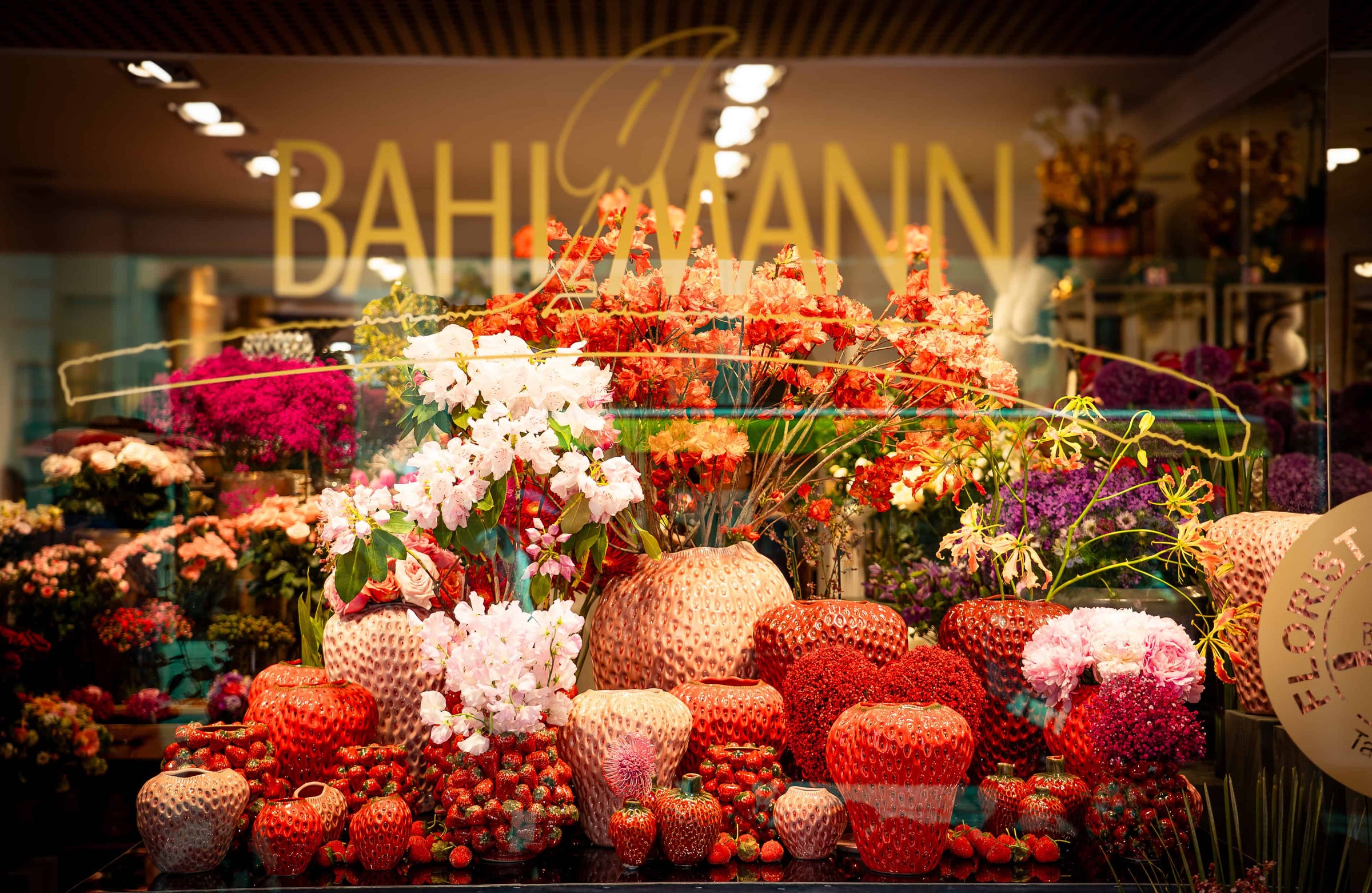 Das Schaufenster von Blumen Bahlmann im Rathaus München, ausgestattet mit einer Vielzahl unterschiedlicher Keramikvasen in Erdbeerform. In unterschiedlichen Großen, Formen und Farben.