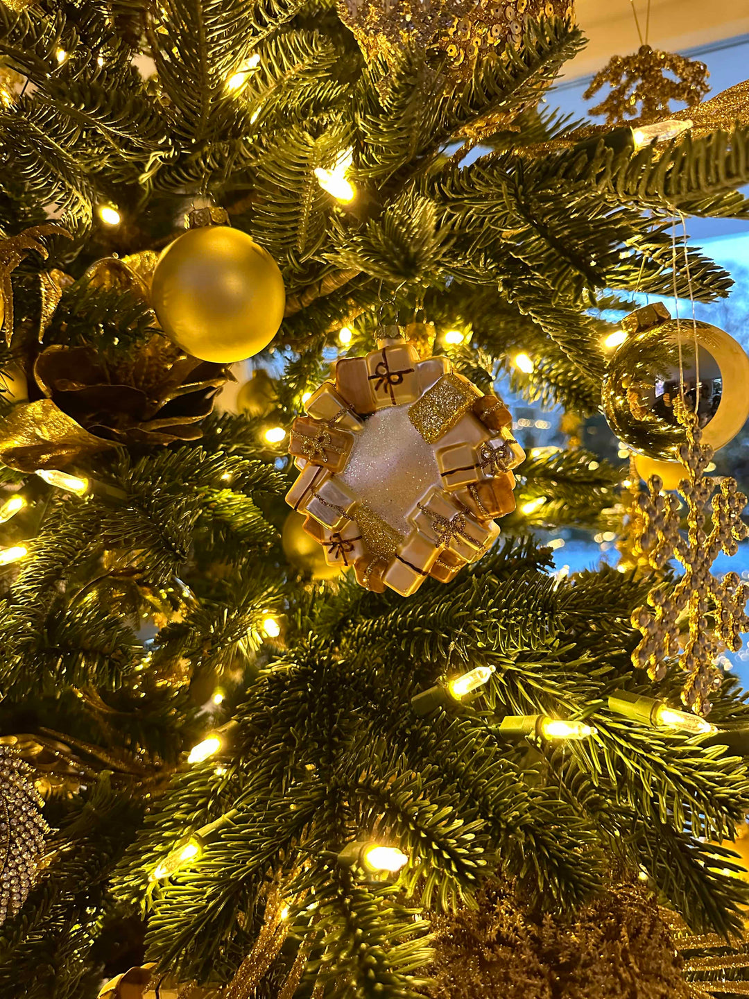 Detailaufnahme eines Glas-Ornamentes, das eine Kugel darstellt, um die viele kleine Geschenke gelegt sind. Bereitgestellt von Blumen Bahlmann in München.
