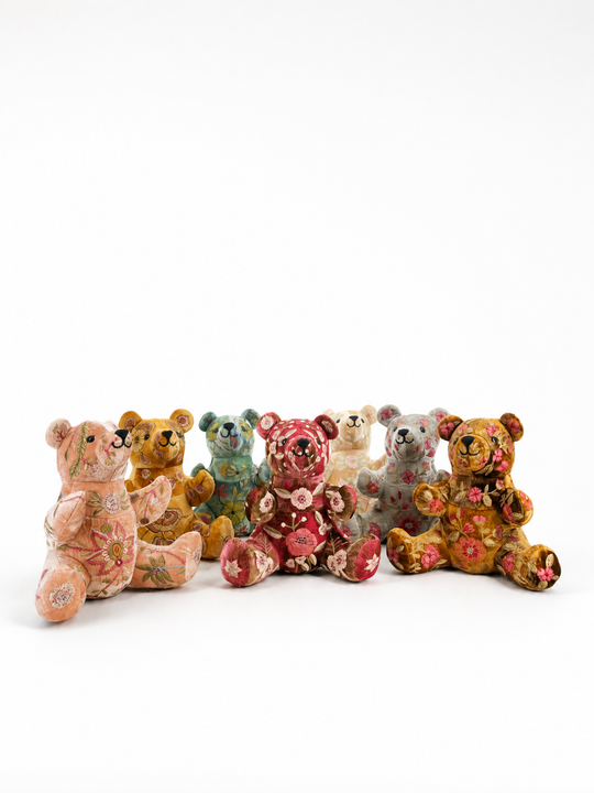 Sieben große Anke Drechsel Deko-Teddybären aus bestickem Samt in Quarzrosa, Canyon Gold, Horizon, Burgunderrot, Champagnerfarben, Blaugrau und Braun, sitzend nebeneinander von vorne – Blumen Bahlmann München