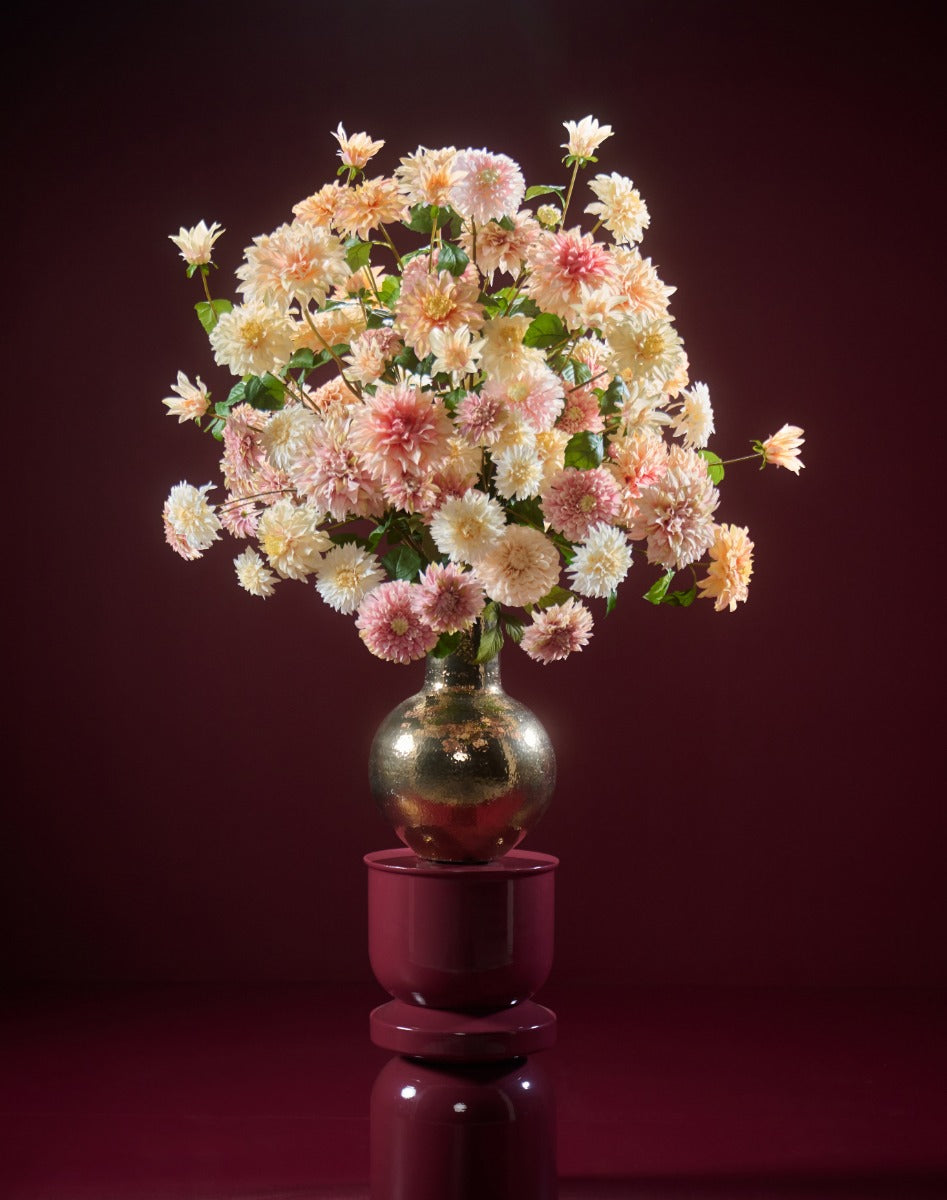 Üppiges Seidenblumenarrangement mit Dahlien in Creme, Apricot und Rosé in einer bauchigen goldfarbenen Vase. Blumen Bahlmann München