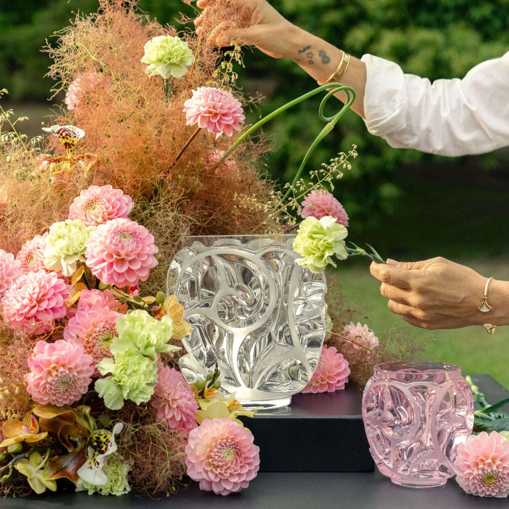 Runde Tourbillons Kristallvase von Lalique mit transparentem Glanz und kunstvoll geschwungenen Wirbelmotiven, umgeben von Blumen. Blumen Bahlmann München