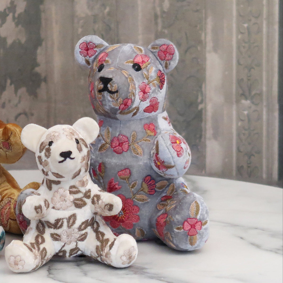 Handgestickter Teddybär in Blaugrau von Anke Drechsel aus weichem Stoff mit liebevollen Details, sitzend mit freundlichem Gesichtsausdruck. Blumen Bahlmann München