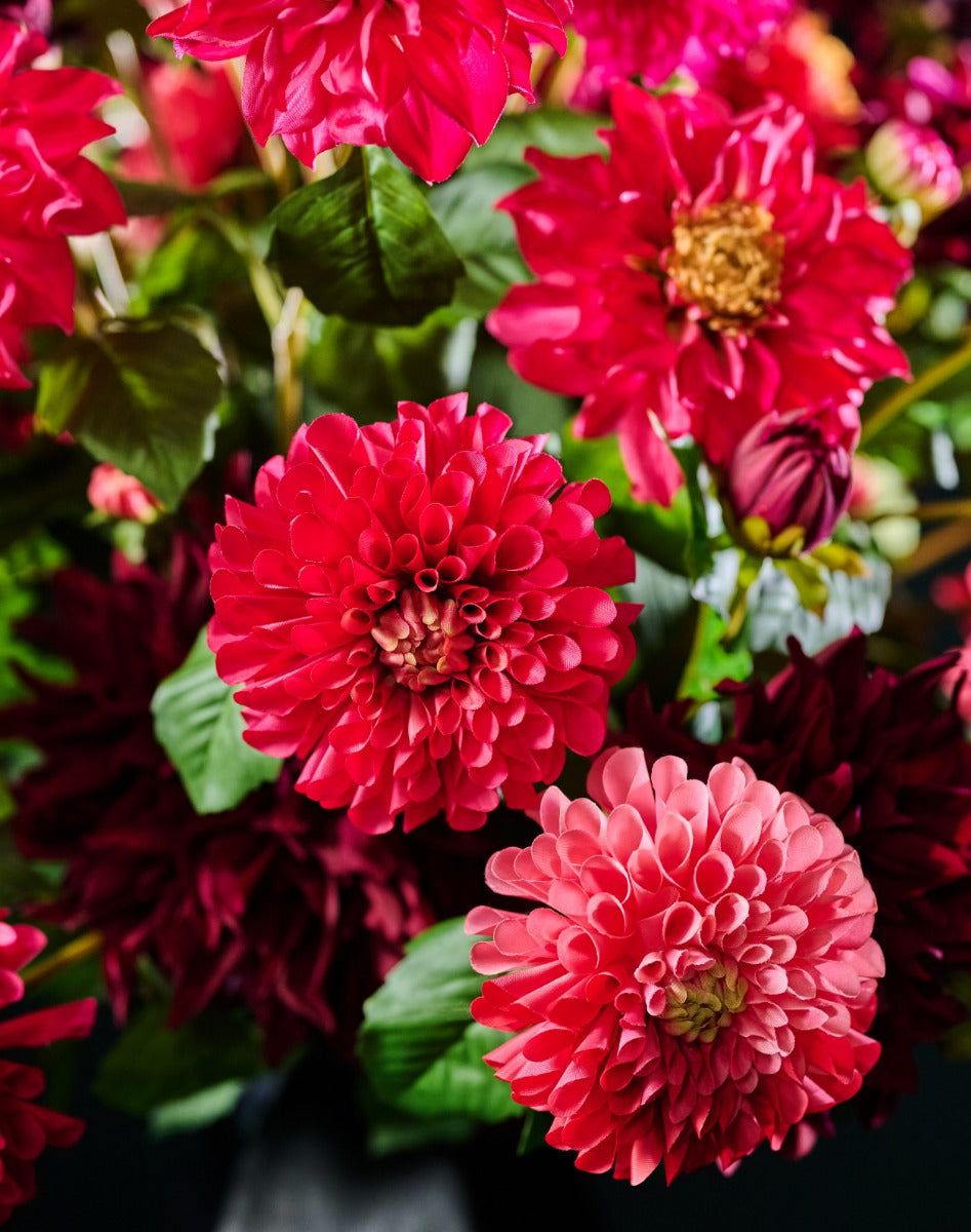 Opulentes Seidenblumengesteck mit verschieden geformten Dahlienblüten in Pink, Rot und dunklem Bordeaux. Blumen Bahlmann München.