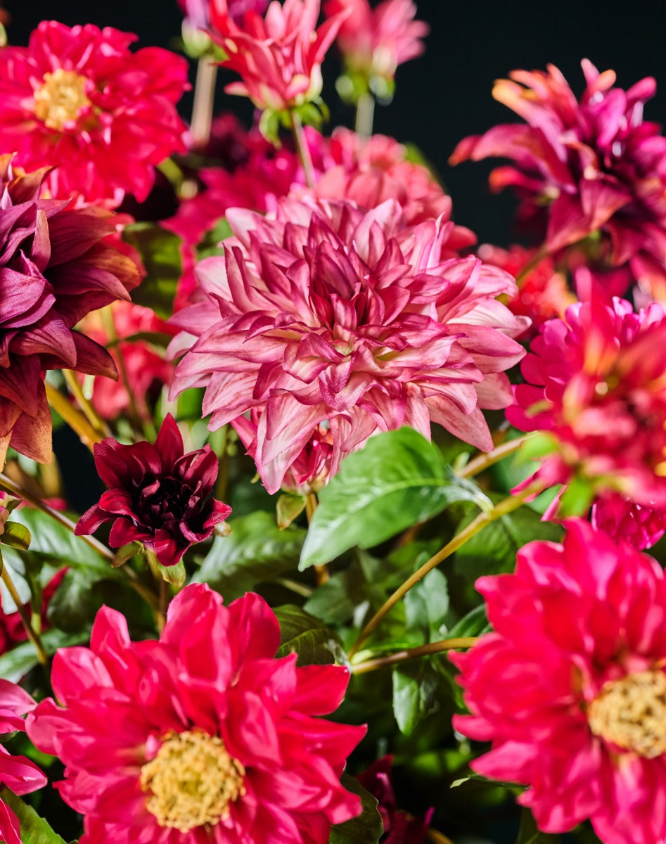 Elegantes Kunstblumenarrangement mit leuchtenden Dahlien und frischem Grün in einer strukturierten schwarzen Vase. Blumen Bahlmann München.