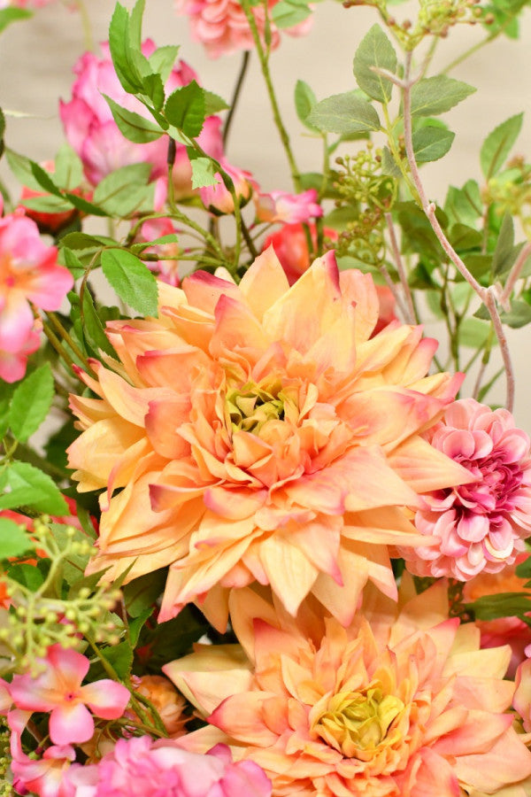 Farbenfrohes Seidenblumengesteck mit üppigen Blüten und ausladenden grünen Zweigen in einer glänzenden rosafarbenen Vase. Blumen Bahlmann München