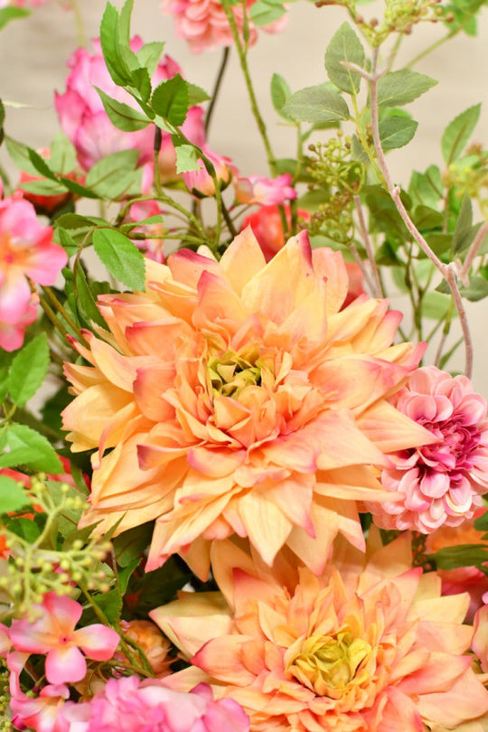 Farbenfrohes Seidenblumengesteck mit üppigen Blüten und ausladenden grünen Zweigen in einer glänzenden rosafarbenen Vase. Blumen Bahlmann München