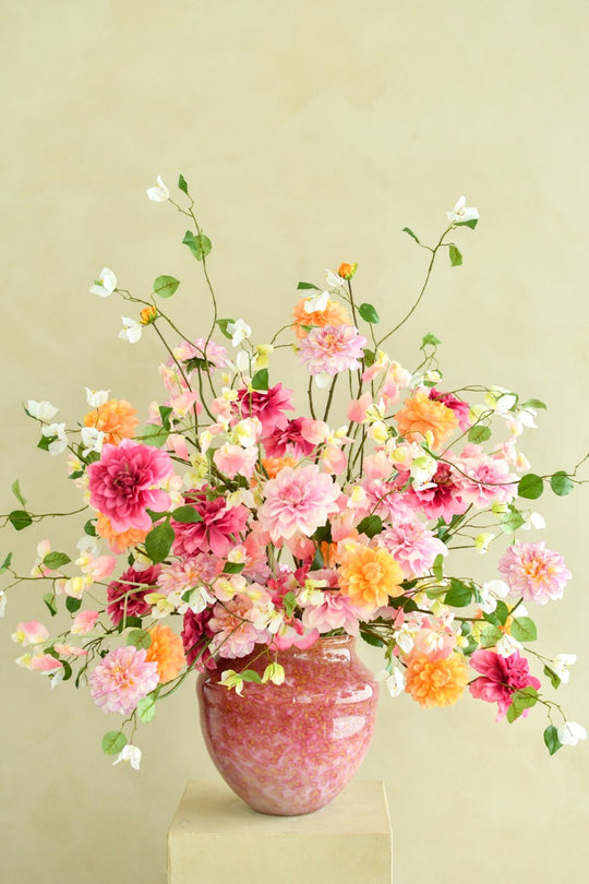 Üppiges Seidenblumenarrangement in Pink, Rosé, Apricot, Orange und Creme mit locker geschwungenen Zweigen in einer rosafarbenen Vase. Blumen Bahlmann München