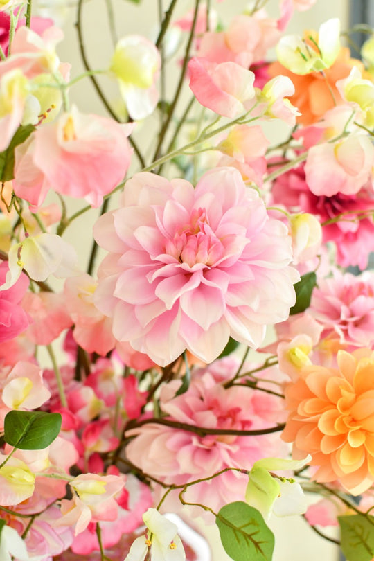 Farbenfrohes Seidenblumengesteck mit rosa, pinken und orangefarbenen Blüten sowie filigranen weißen Blütenzweigen. Blumen Bahlmann München