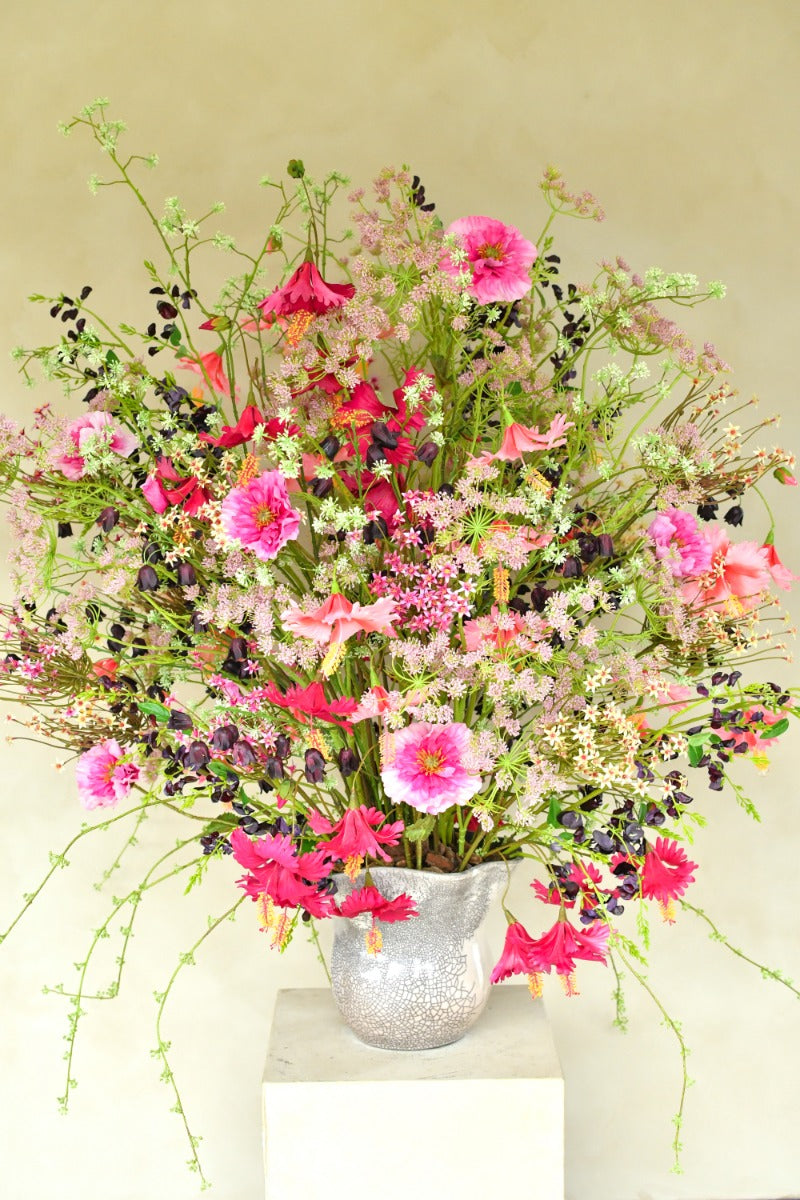 Üppiges Seidenblumenarrangement in Pink, Fuchsia, Rosé und Violett mit filigranen Zweigen in einer silberfarbenen Vase. Blumen Bahlmann München