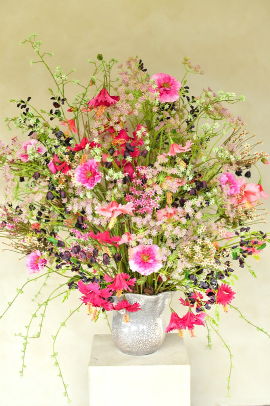 Üppiges Seidenblumenarrangement in Pink, Fuchsia, Rosé und Violett mit filigranen Zweigen in einer silberfarbenen Vase. Blumen Bahlmann München