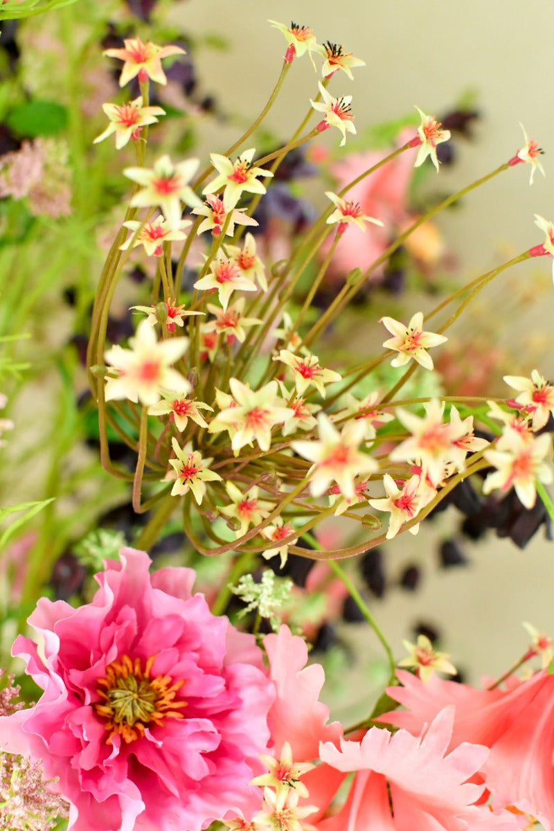 Natürlich wirkendes Kunstblumenarrangement in intensiven Rosatönen mit feinen Wiesenblüten und strukturierter silberner Vase. Blumen Bahlmann München