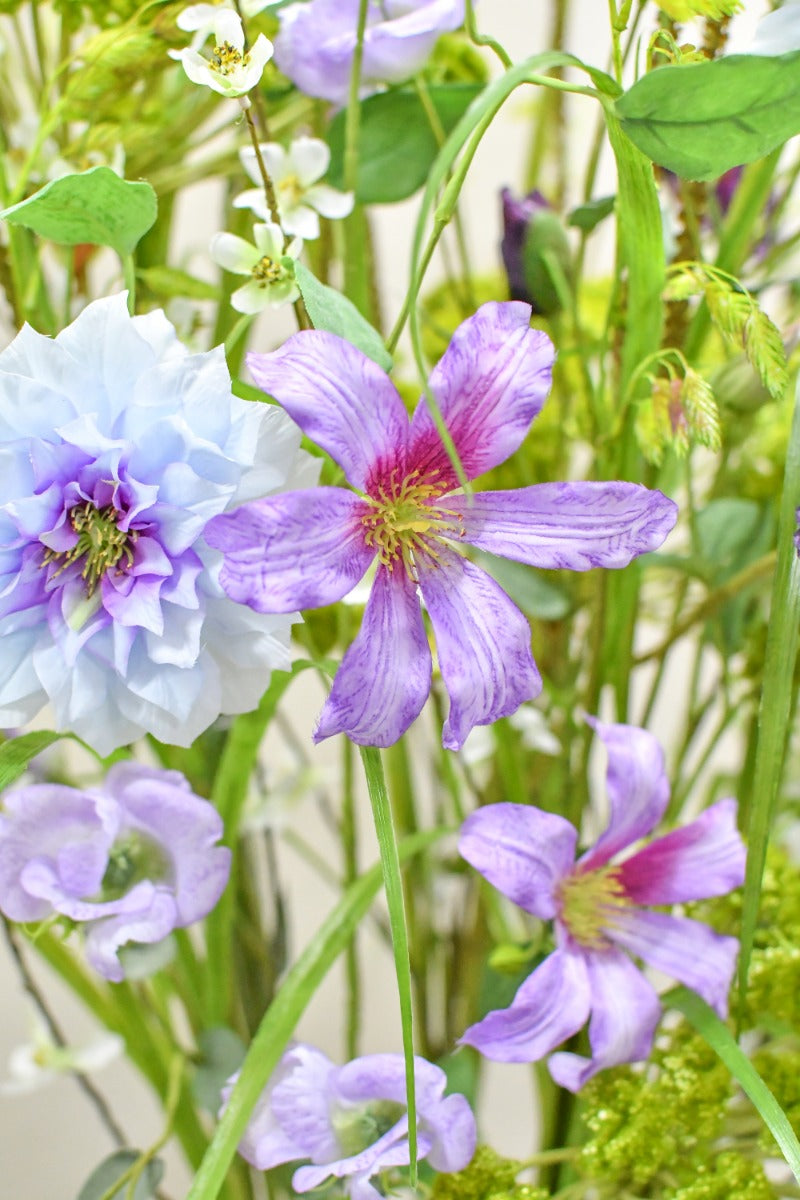 Natürlich wirkendes Seidenblumen-Gesteck mit fliederfarbenen Blüten und filigranen Zweigen von Blumen Bahlmann München.