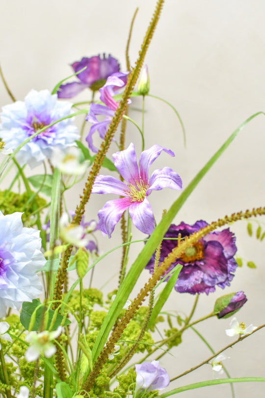 Hochwertiges künstliches Blumengesteck mit zarten Blüten, Gräsern und grünen Akzenten von Blumen Bahlmann München.