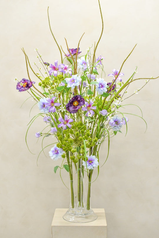 Luftiges Seidenblumenarrangement in Flieder, Blau und Grün in transparenter Glasvase von Blumen Bahlmann München.